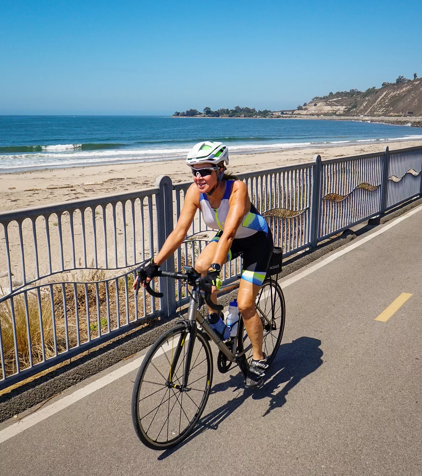 Guest cycling down beach road, ocean, sand behind her.