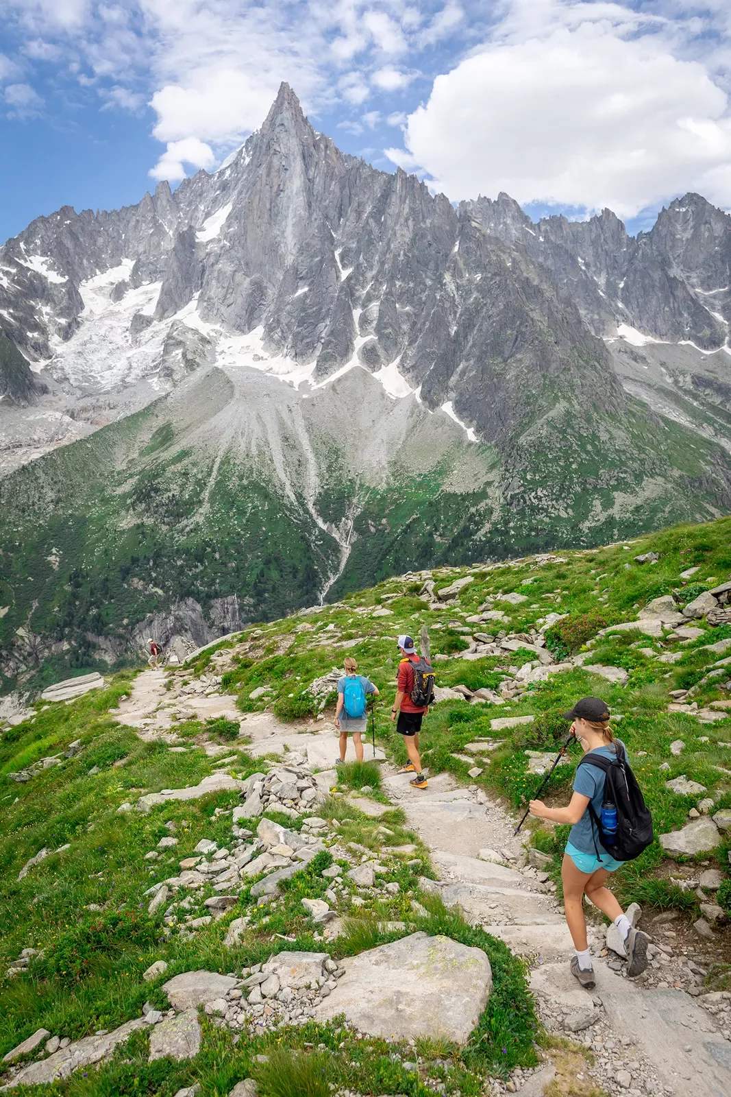 Three guests walking down mountainside, large, spiky peaks in distance.