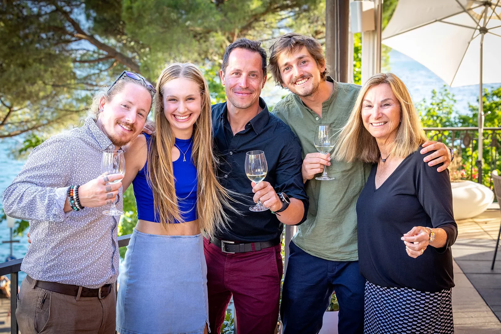 Five guests in nice clothes, wine glasses in hand smiling at camera.