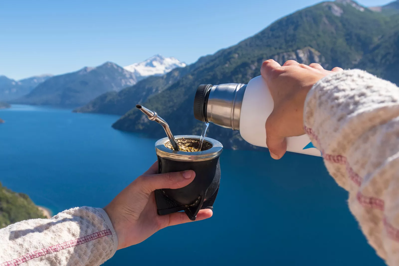 Hand pouring water into a mate, with a large lake in the background