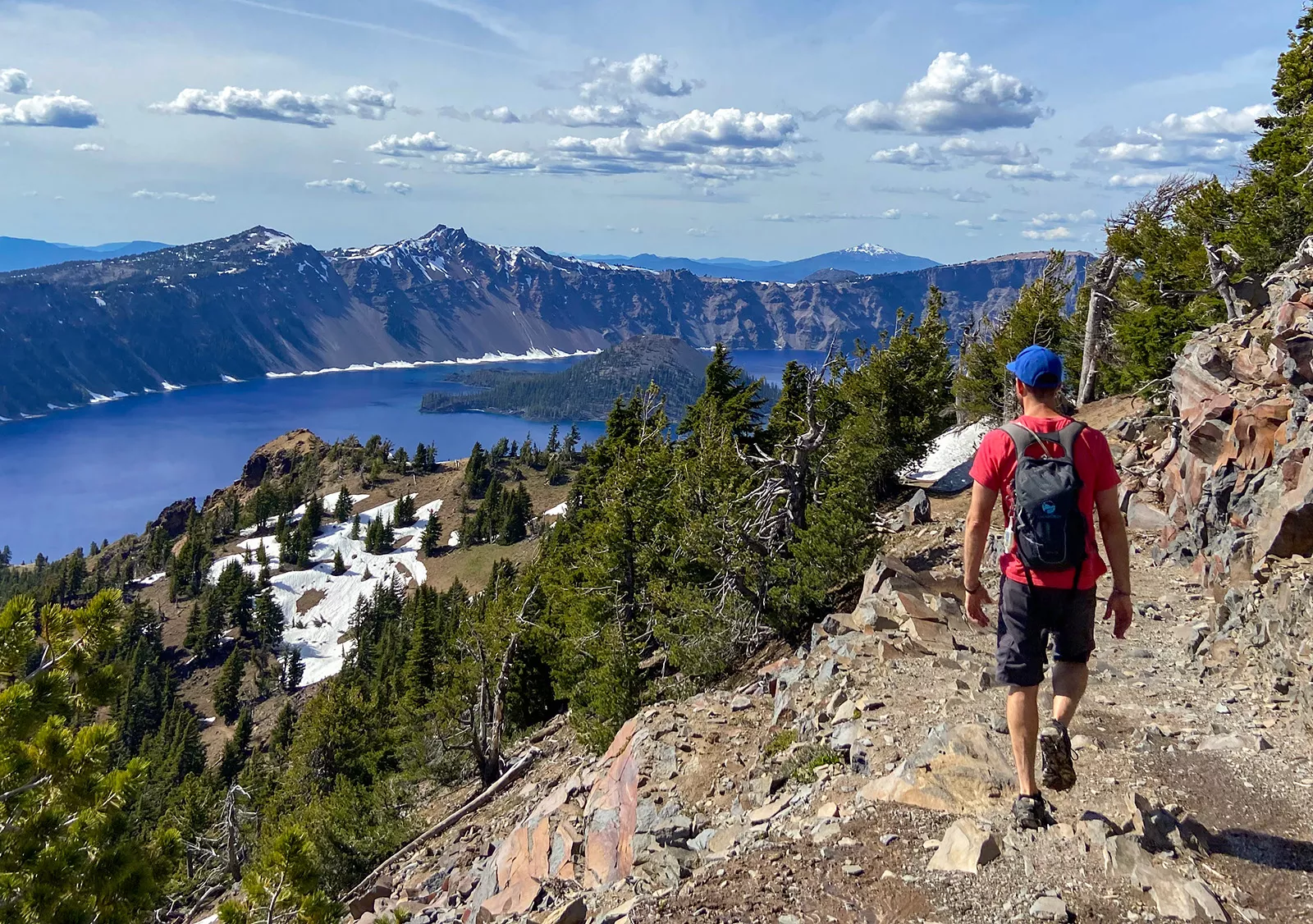 Man hiking of a stone and gravel patch looking down at a lack and valley of trees