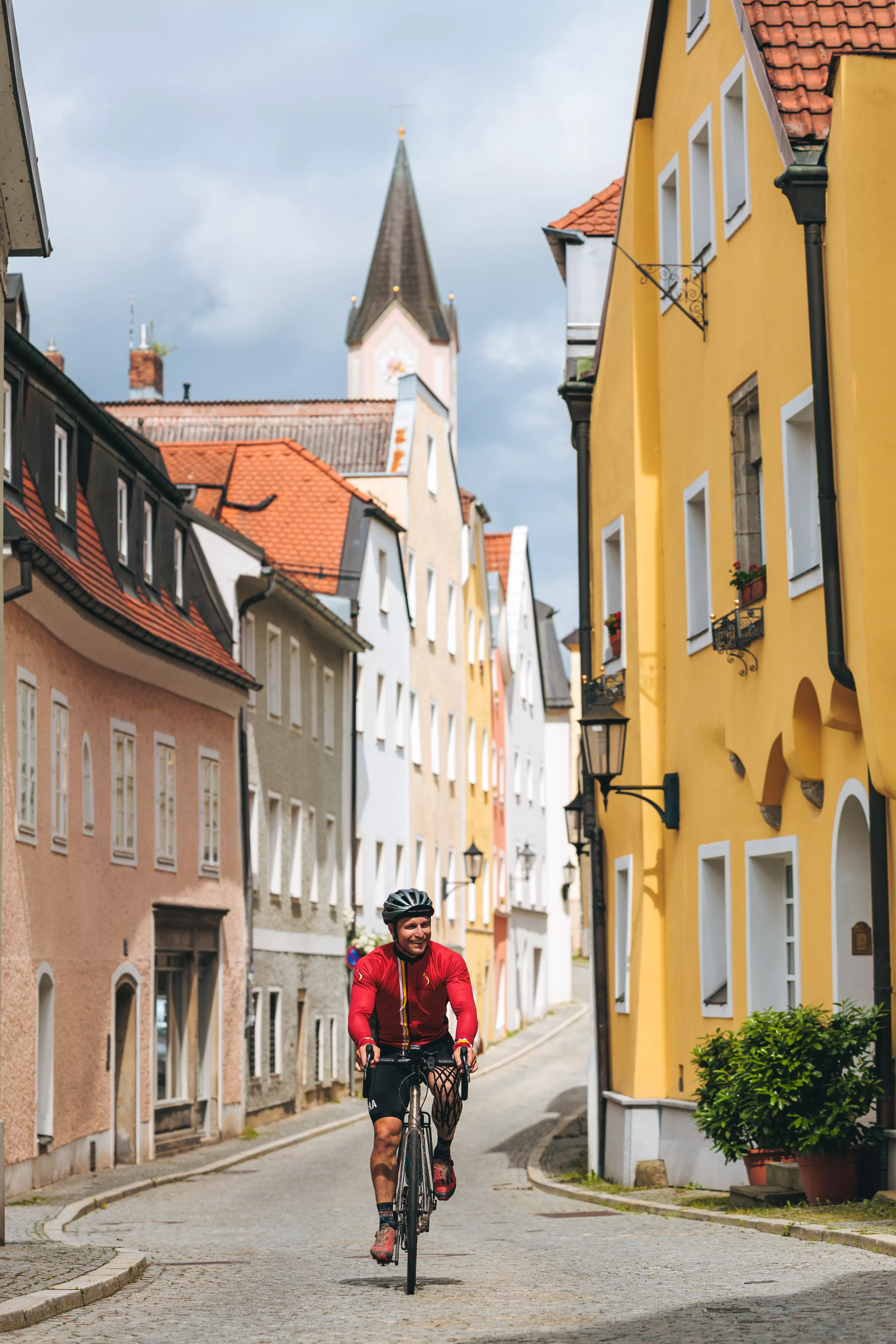Man in red riding a bicycle in an alley of a European town