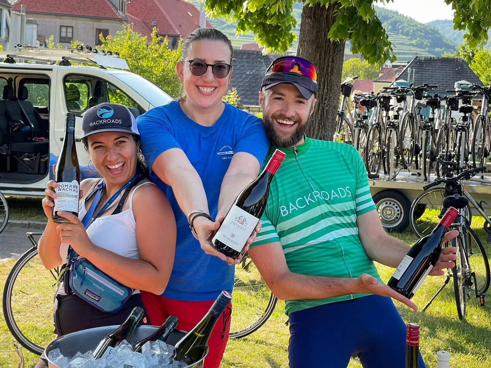 Two women and one man holding bottles of wine