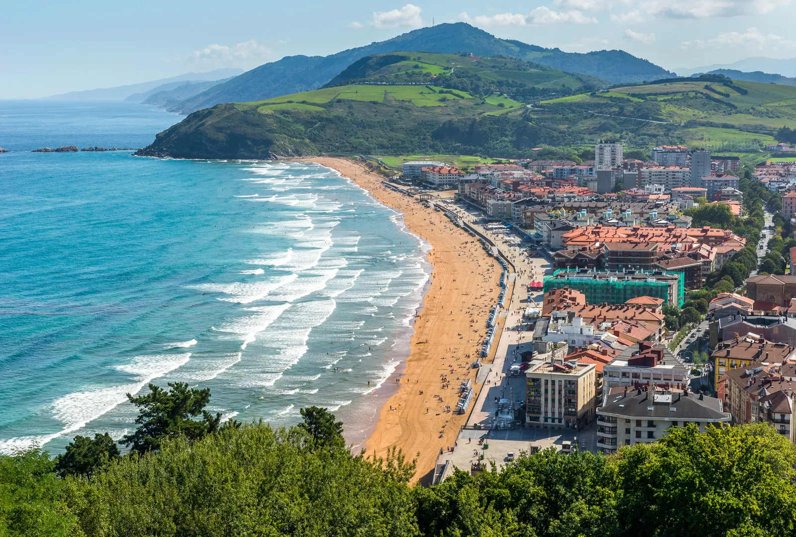 Sky view of a small town next to a beach, with grassy hills in the distance