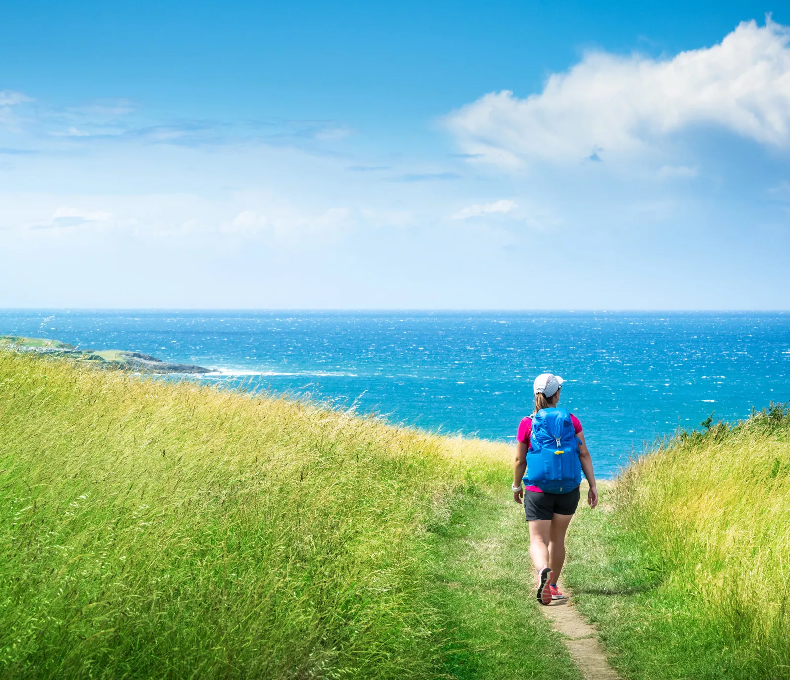 Woman hiking in a grassy field, with the ocean in the distance