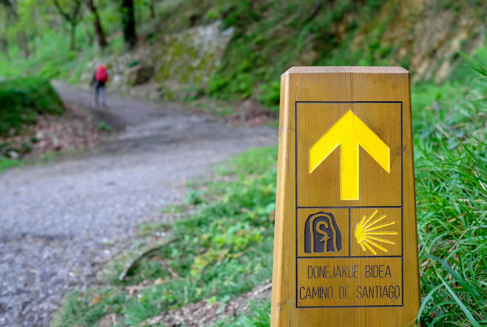 Hiking sign on a trail, with a person walking on a gravel path