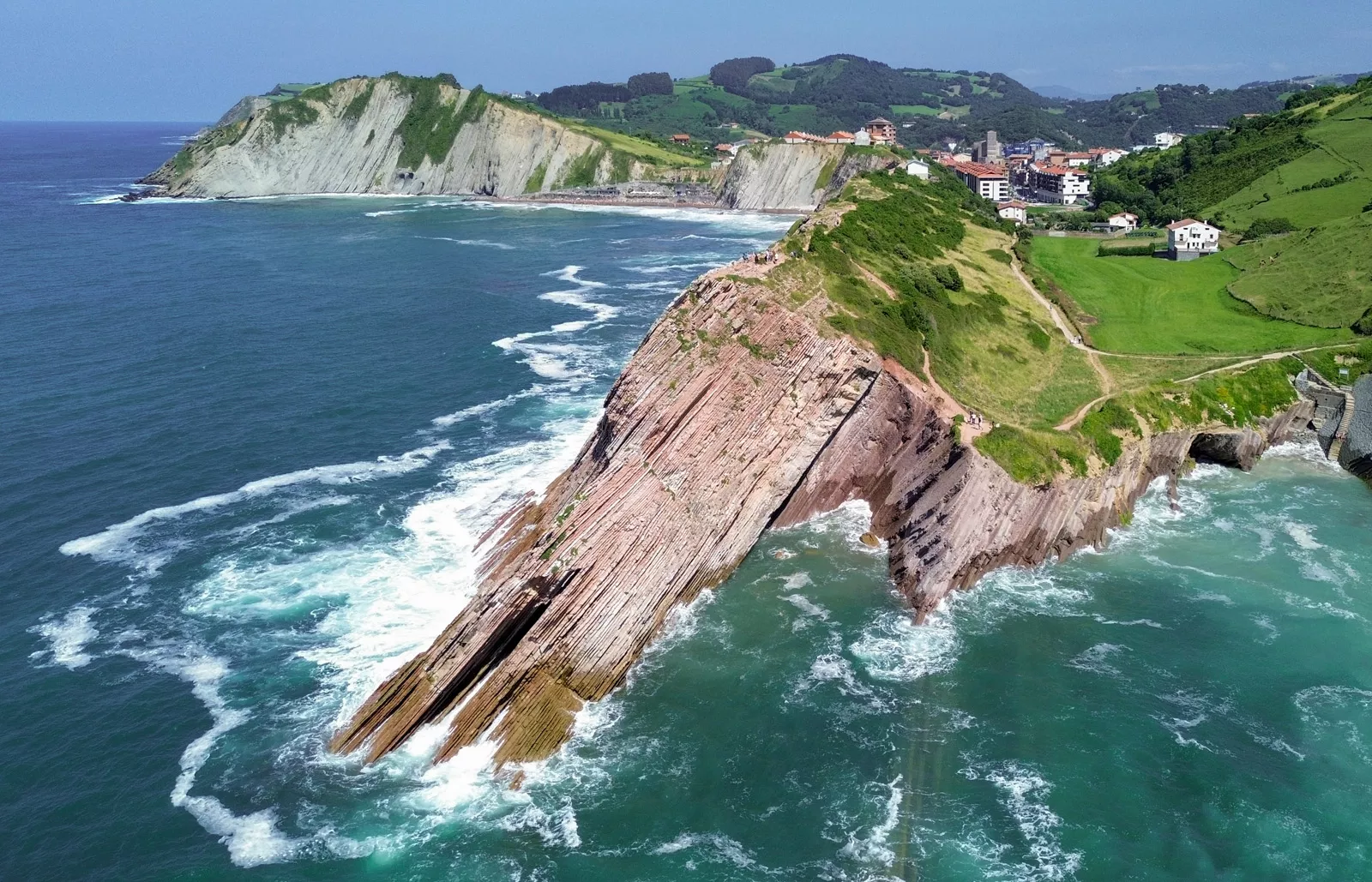 Slanted cliff on the coast of an ocean, with a small town in the distance