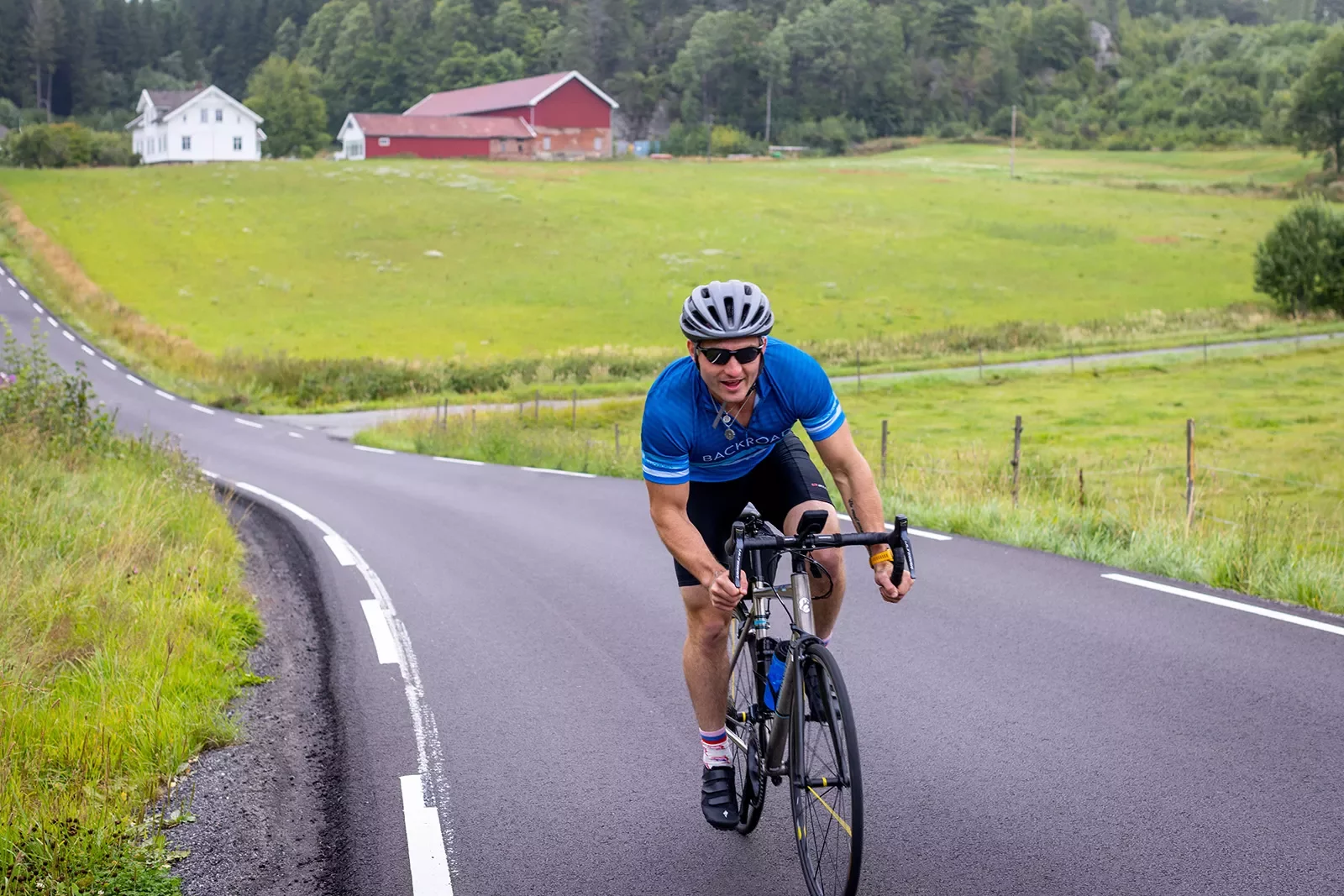 Man riding bike on asphalt road through a grassy field