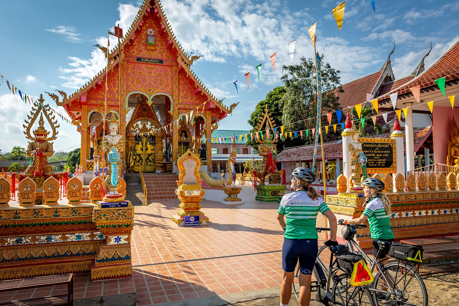 Two women walking their bikes as they approach a shrine