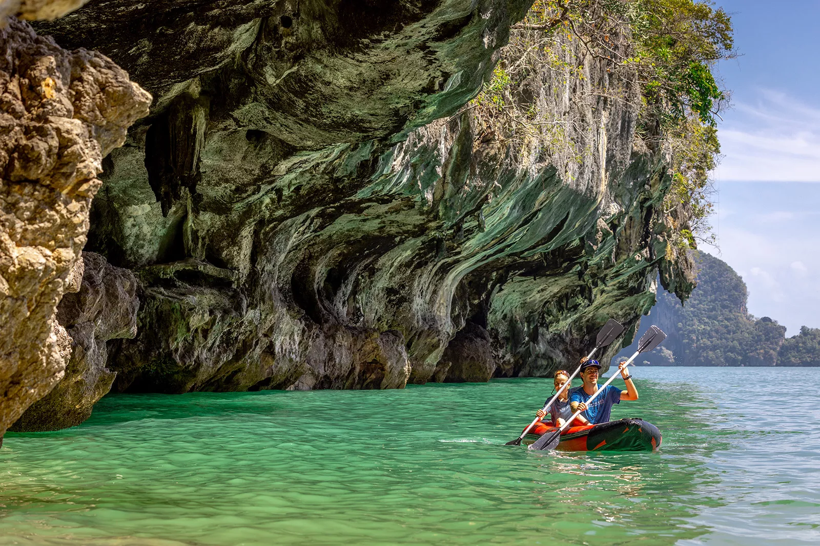 Man and woman paddling in a red kayak in the ocean, under a cliff