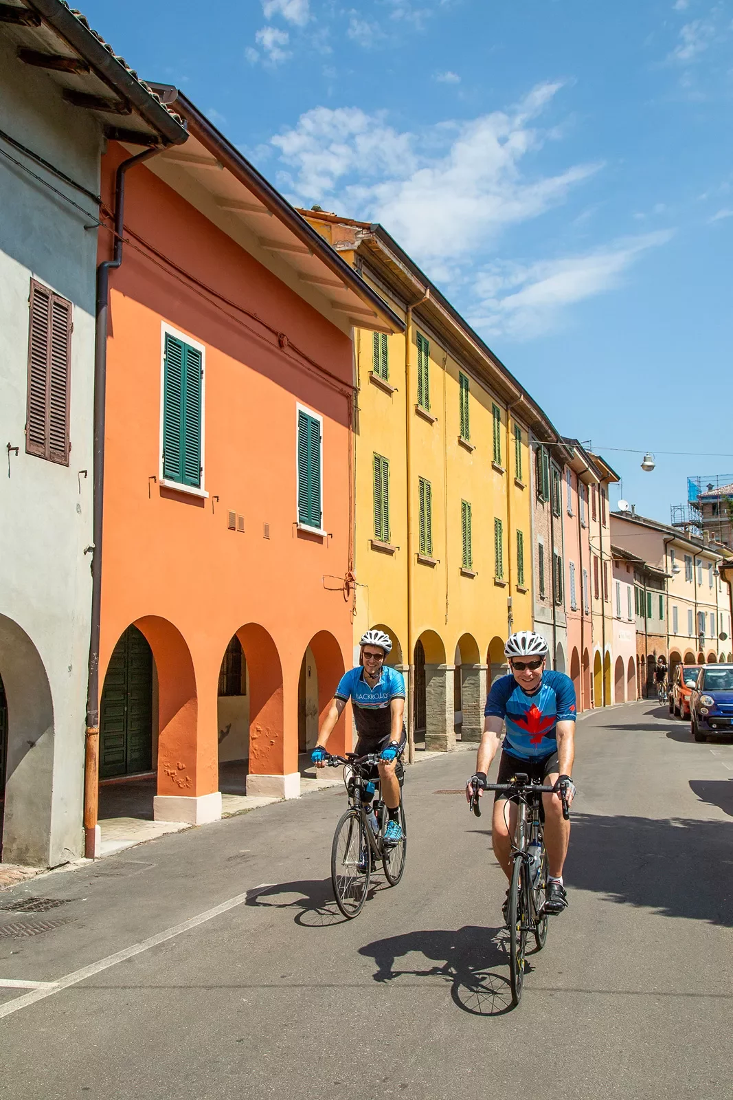 Two bikers on a road next to colorful buildings