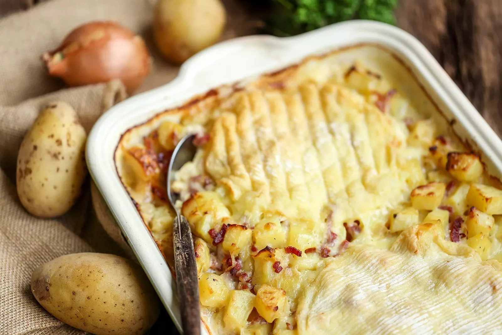 A baking dish with with potatoes and cheese, with a spoon sticking out