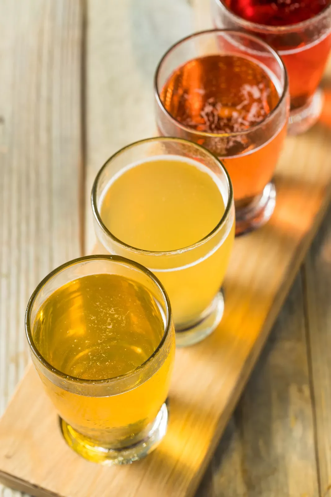 A wooden plank with different cups of beer on it