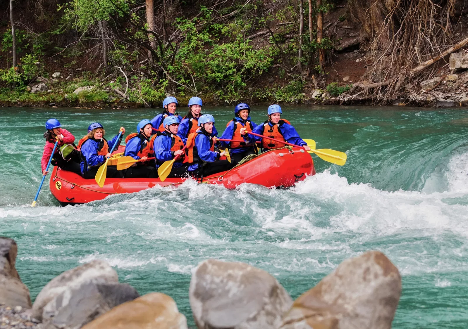 Group of men and women in a red raft paddling through a river