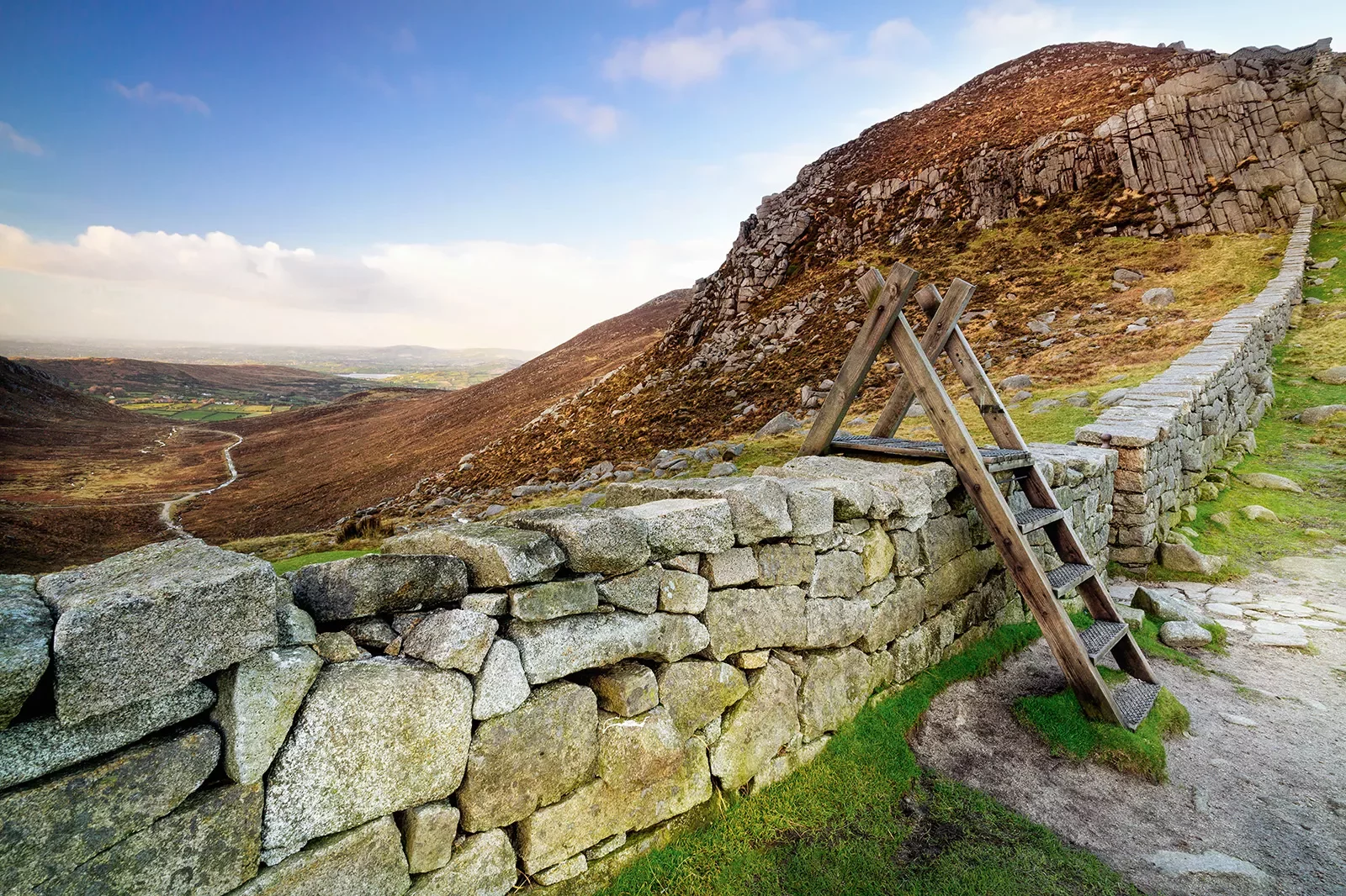 Small wooden latter over a stone barricade overlooking an empty valley