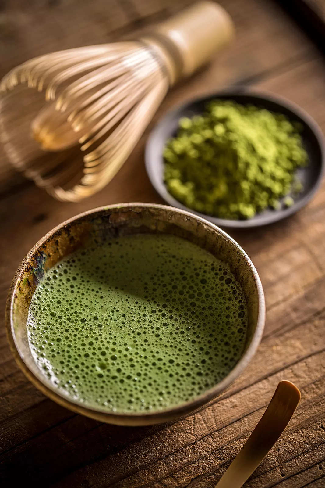 Cup of matcha tea next to a small plate of matcha powder