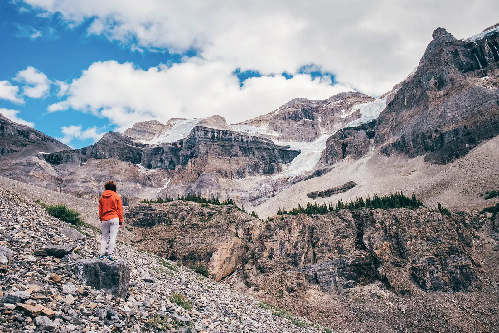 Person on a large rock staring out to large, snowcapped mountains