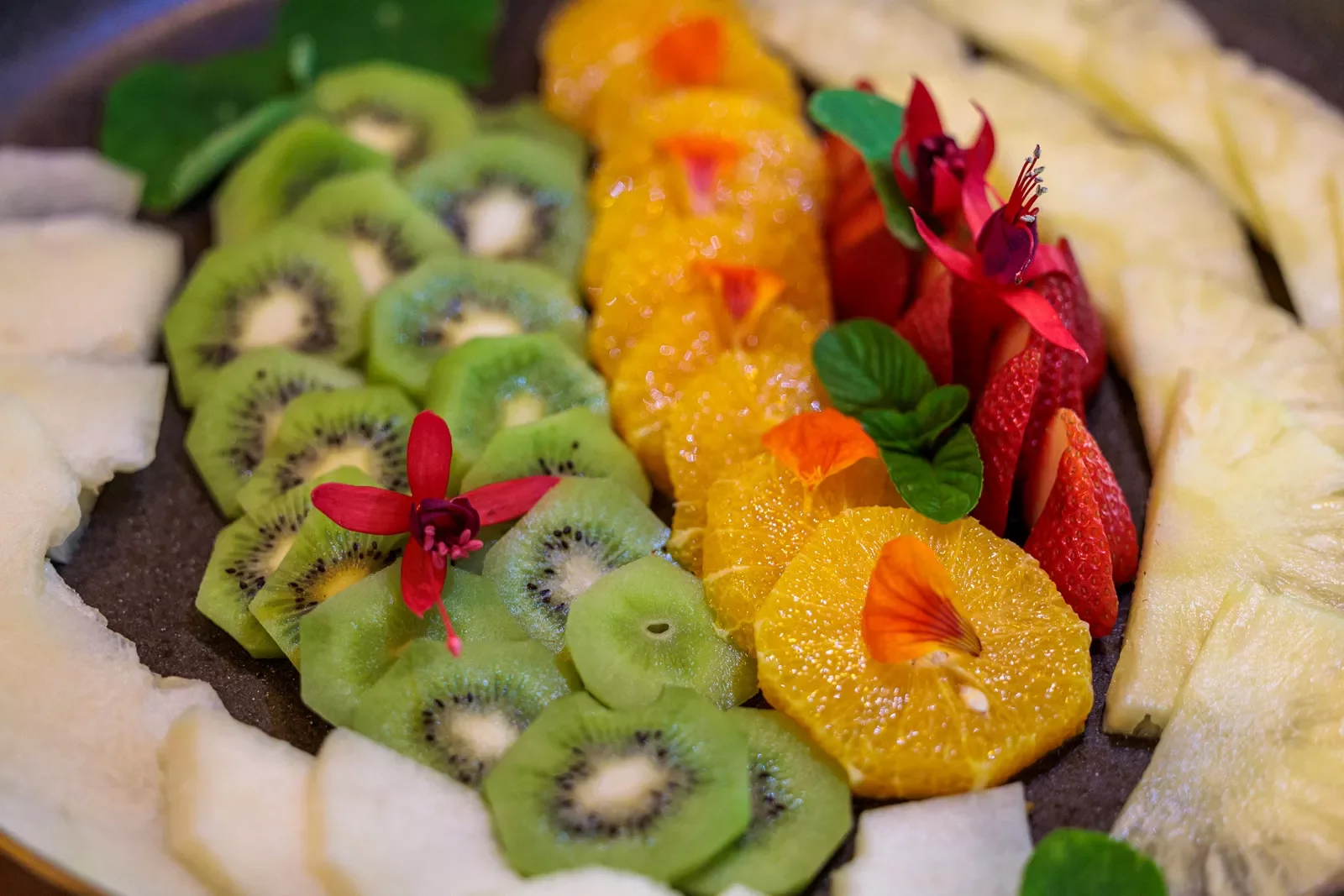 Plate full of sliced fruits, including kiwi, orange, strawberries and pineapple