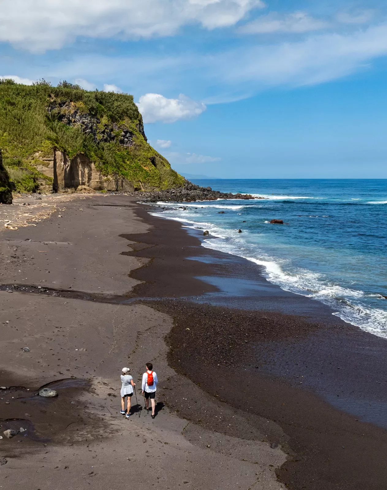 Two people walking on the beach, walking towards a grass-covered cliff