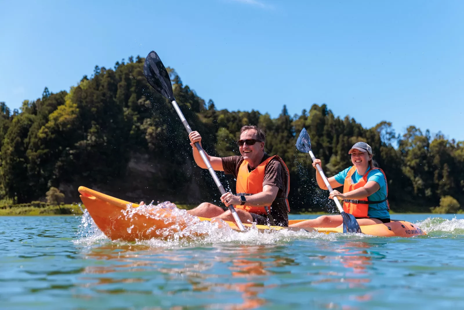 Man and woman smiling in a kayak while paddling in the middle of a lake