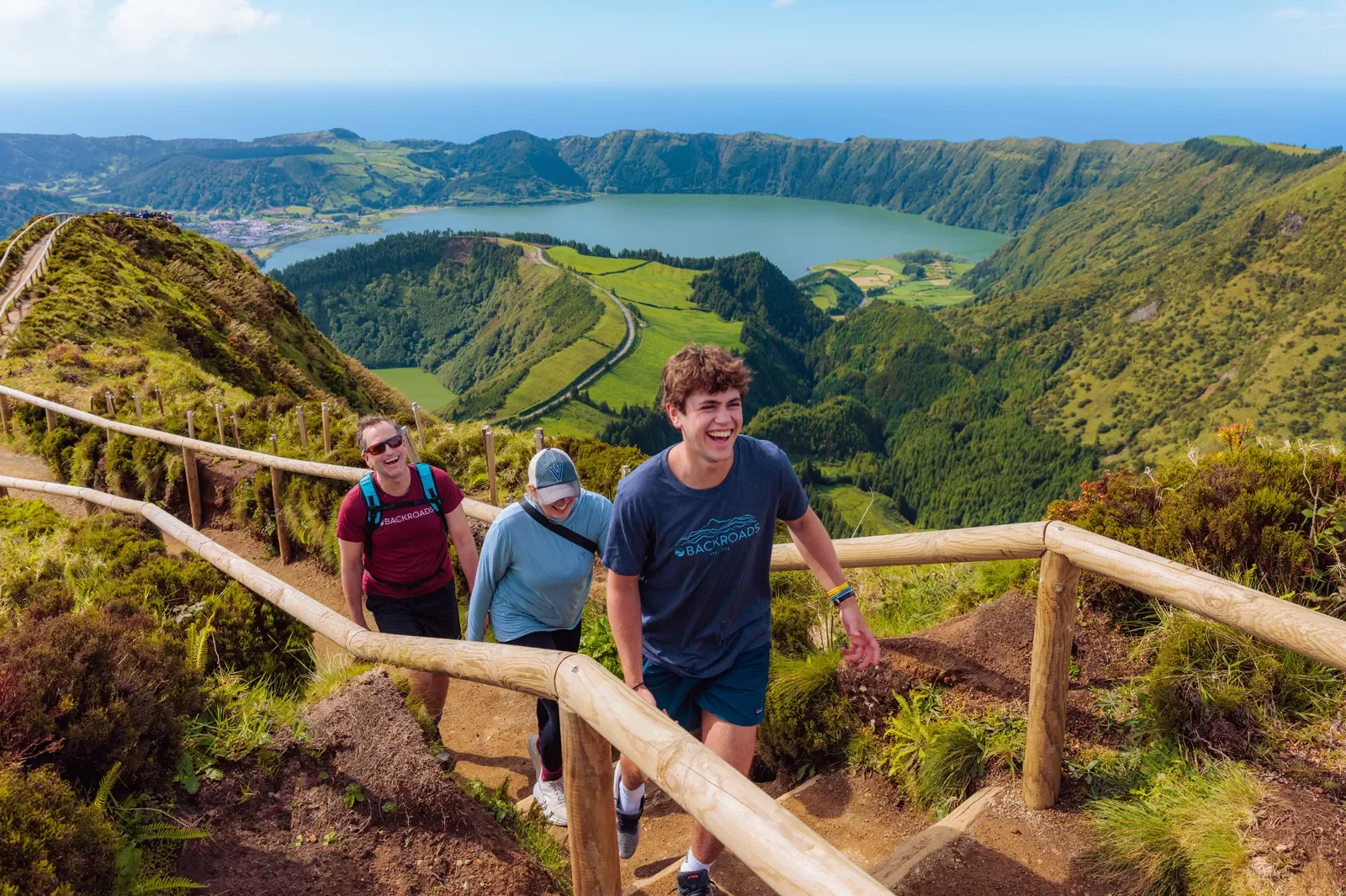 Three people walking on a dirt path that is on top of a hill, with a large valley in the background