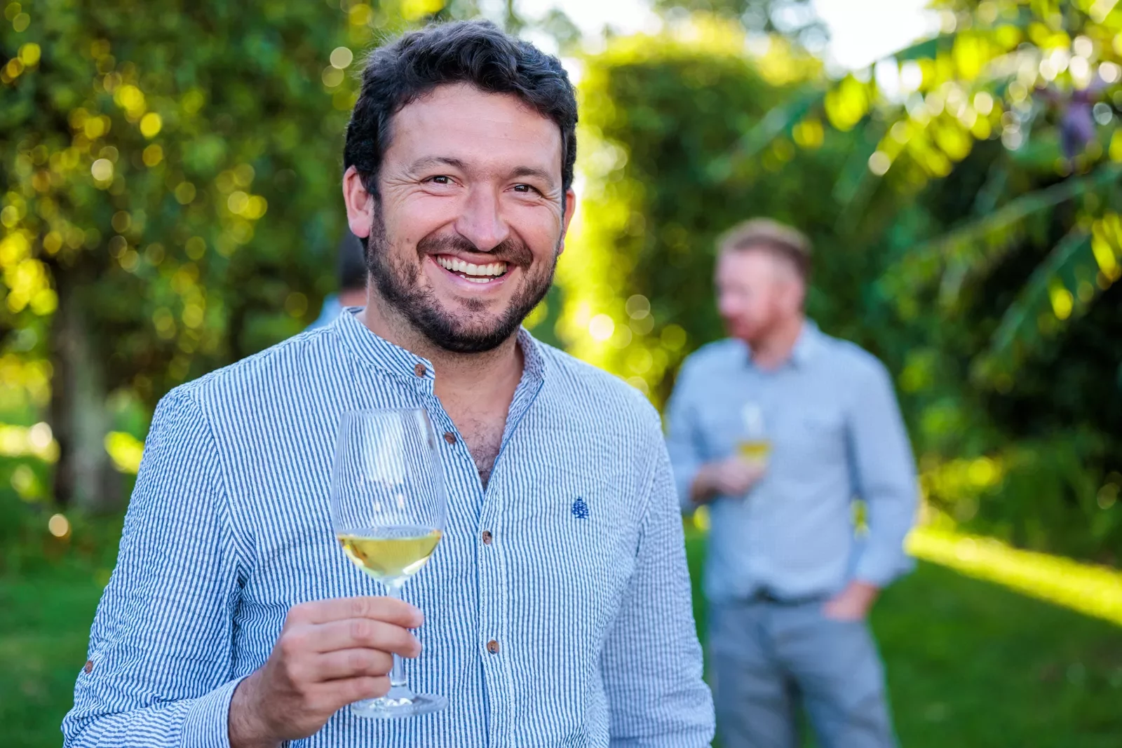 Man smiling at the camera while holding up a glass of wine