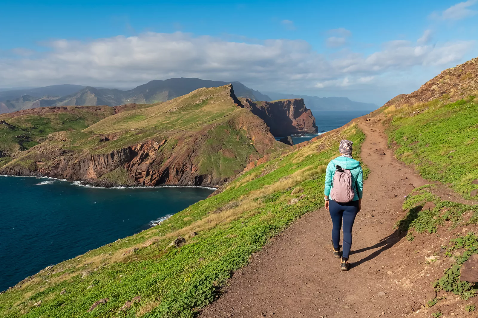 Woman walking on a dirt path on a hill, with a lake on the ground level