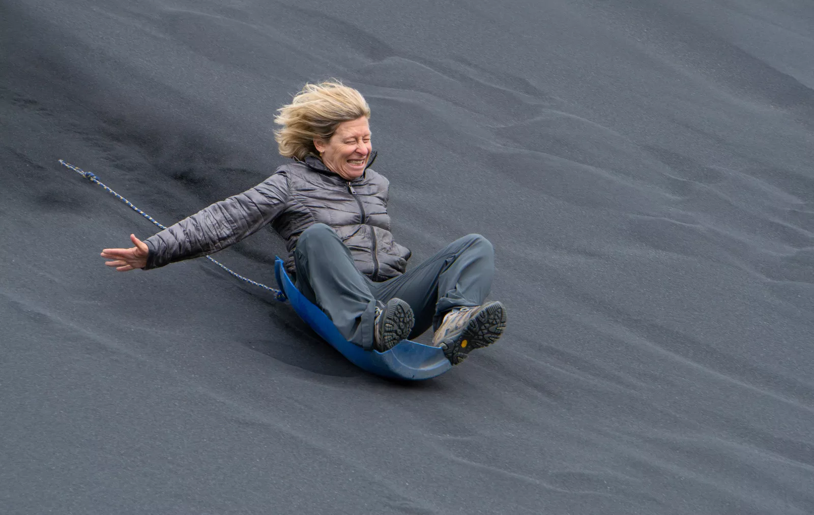 Woman sitting on a plastic barrel seat, going down a sandy hill