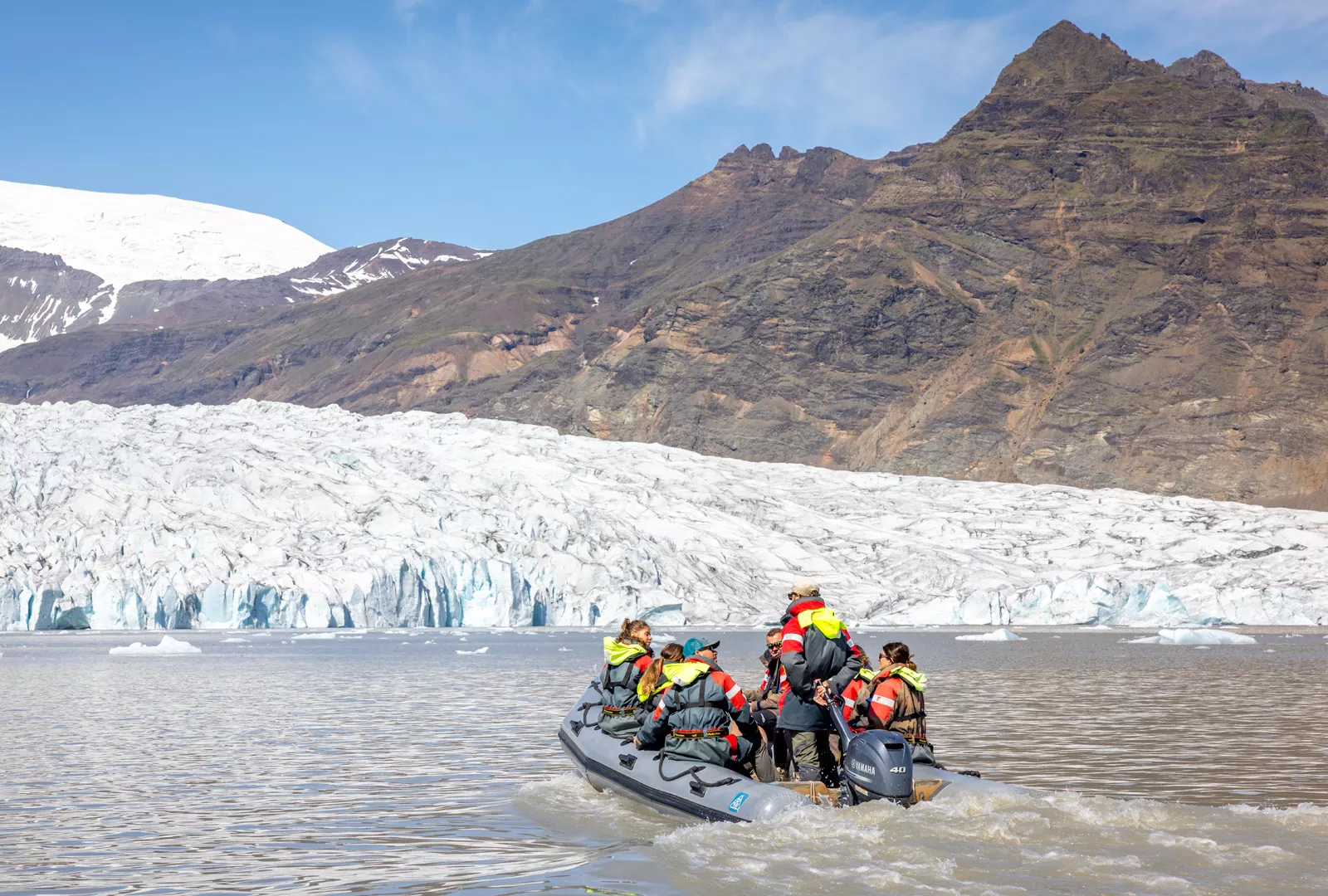 Group of people on a gray raft, going towards snow caps