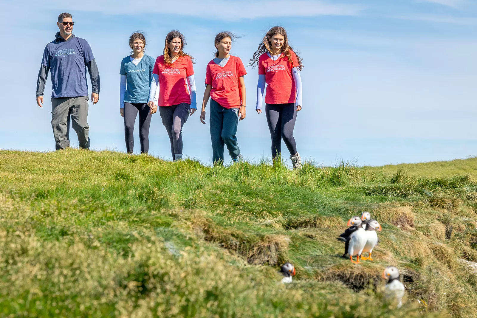 Four women and one man walking on a grassy field