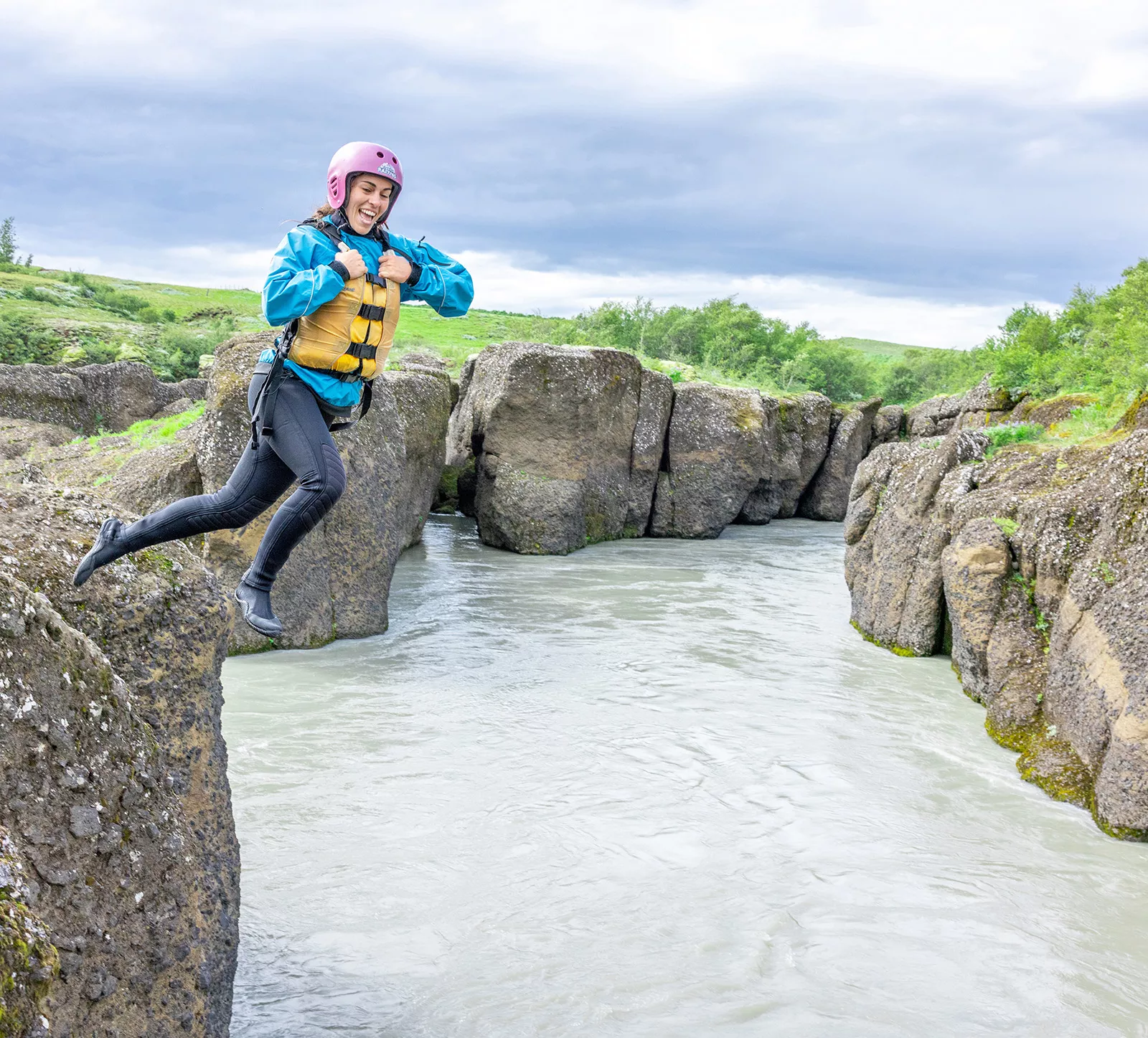 Woman wearing a helmet and life vest jumping into a small lake