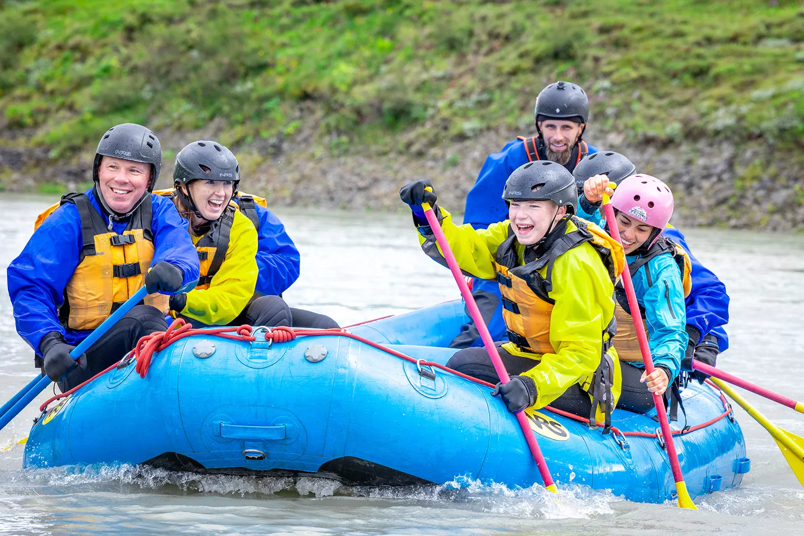 Group of men and women on a blue raft, paddling and smiling