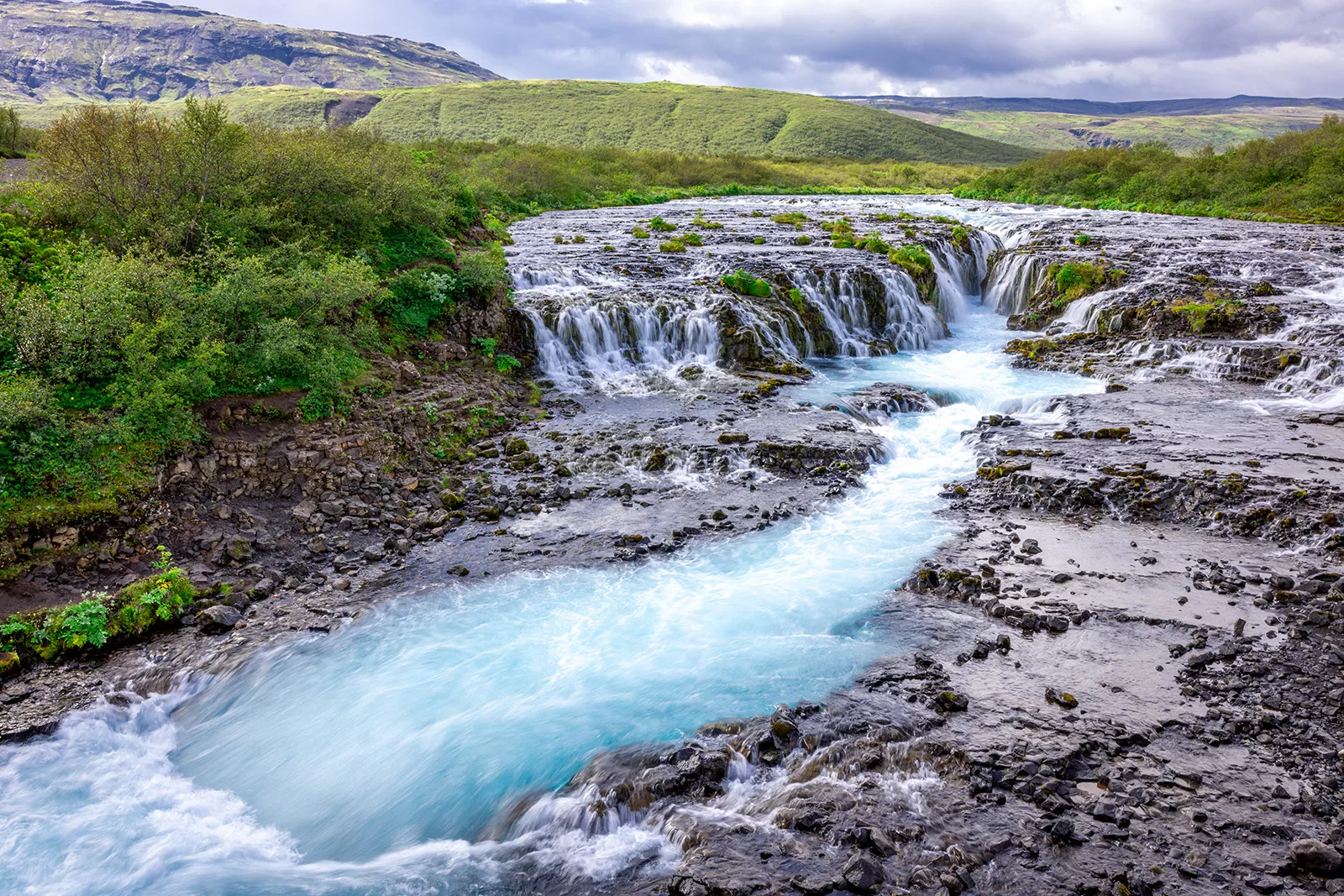 Small waterfall with an active river in the middle of a grass field