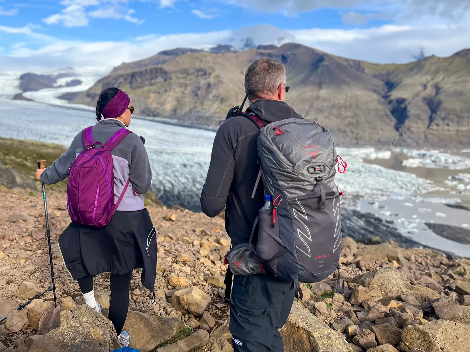 Man and woman hiking on a rock-filled path with a frozen lake to the right