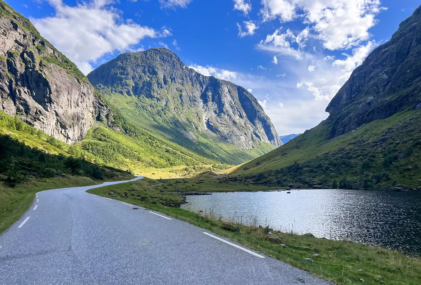 Asphalt road cutting through mountains with a lake to the right