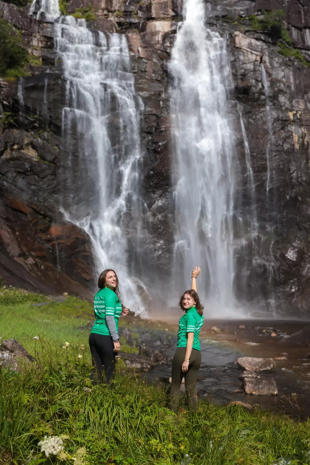 Two guests in bike jerseys pose with a waterfall