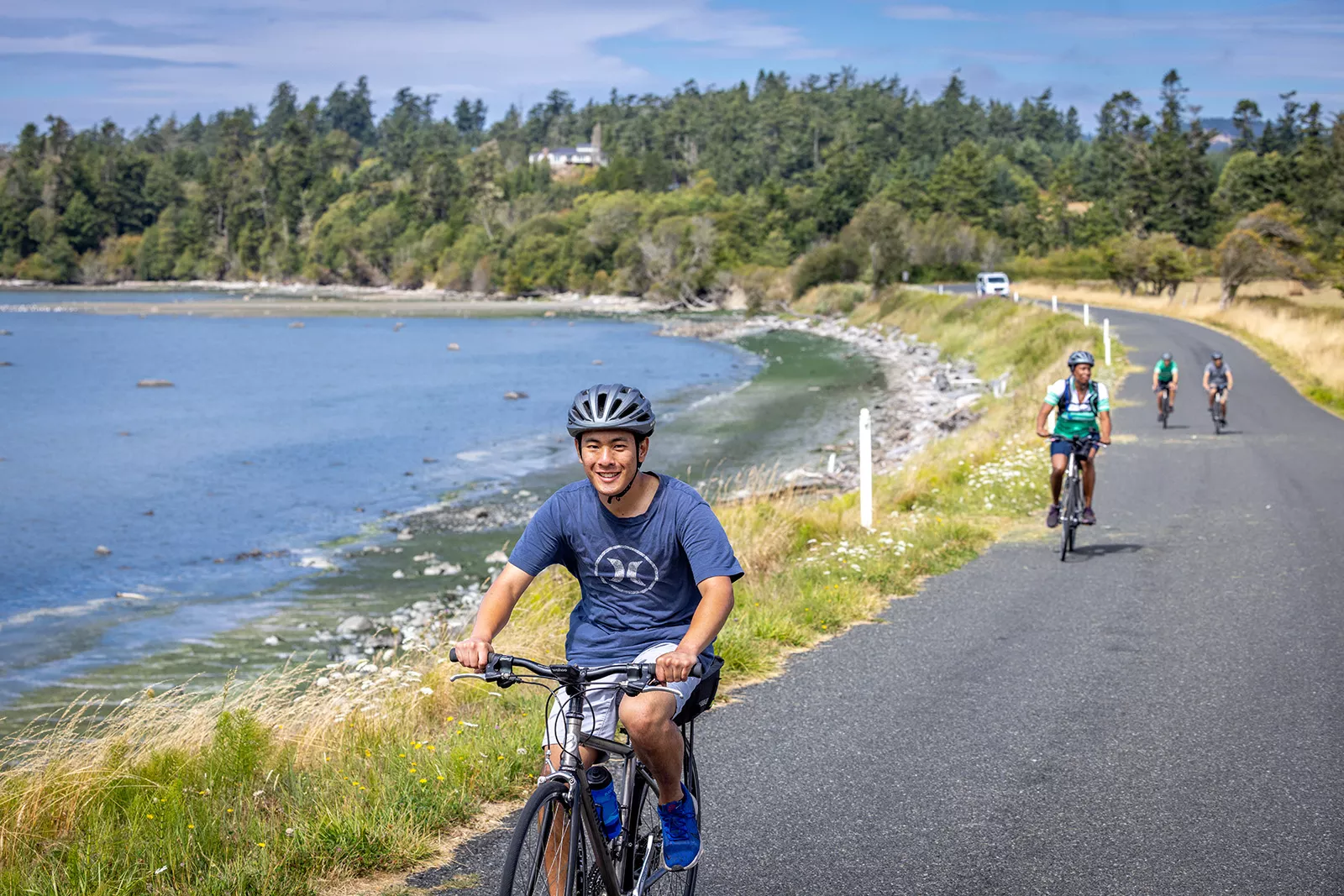 Man riding a bike on an asphalt road with a lake behind him