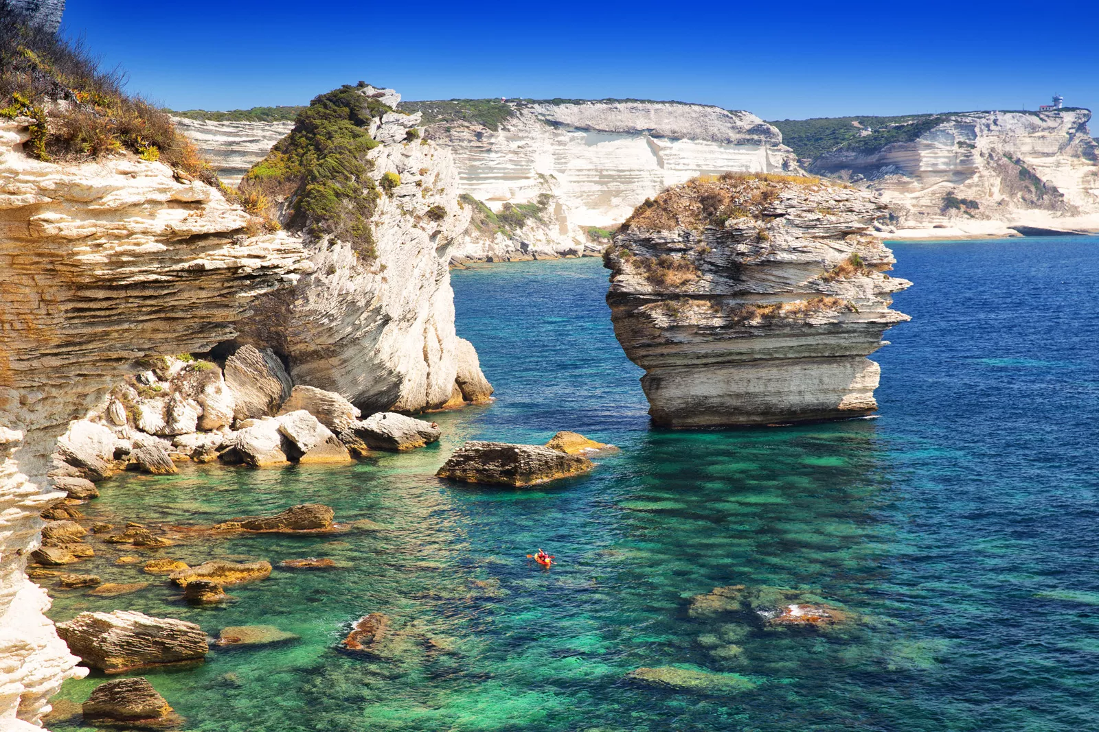 Jagged cliffs on the edge of an ocean, with a red kayak floating