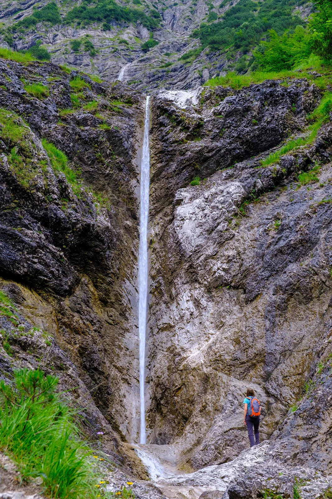 Person looking up at a large cliff with a narrow waterfall