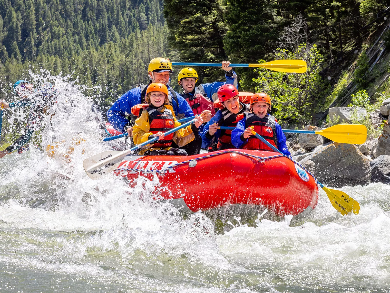 Group of adults and kids on a red raft in the middle of a river