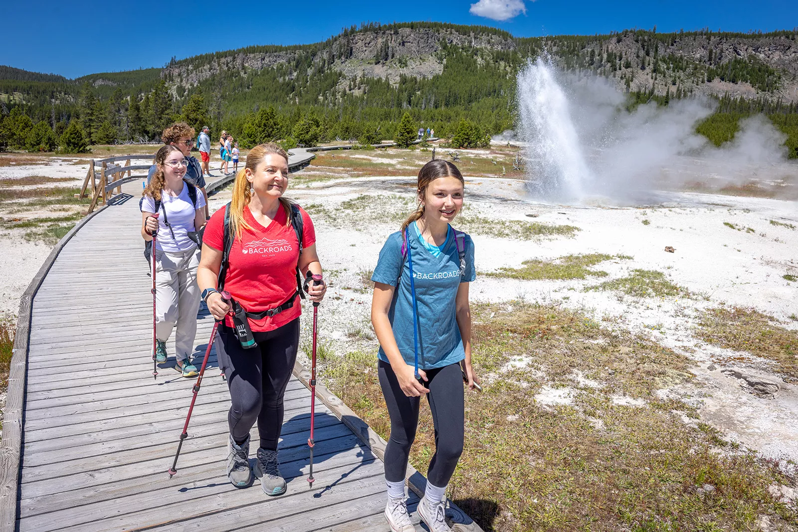 One woman and two girls hiking next to an active geyser