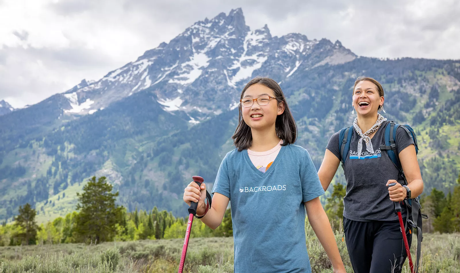 Woman and girl with walking poles hiking in a grassy valley