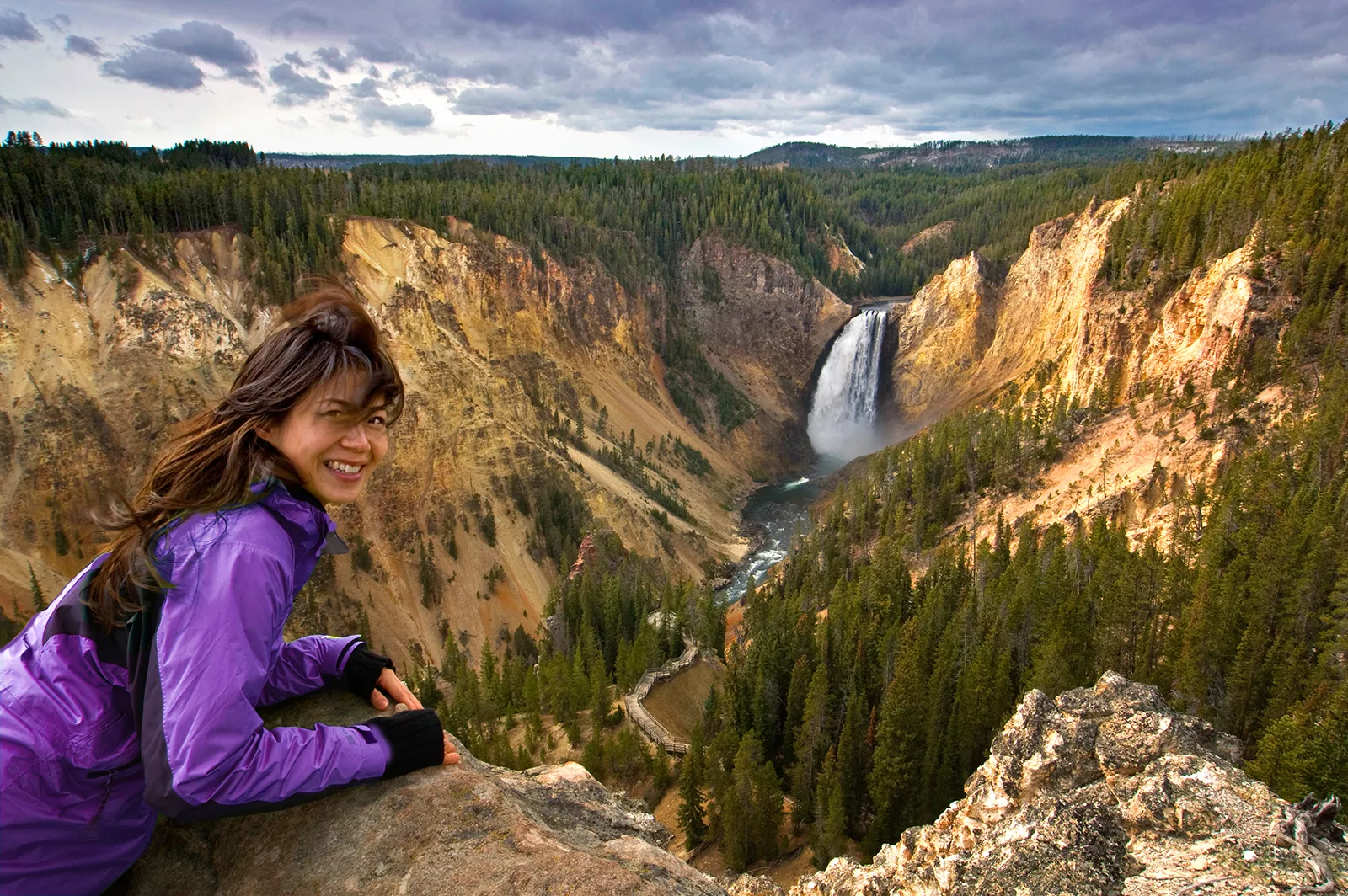 Woman smiling while leaning over a rock on top of a cliff