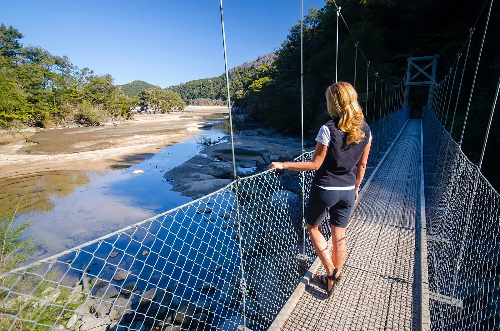 Woman on a metal bridge looking down at a small pond