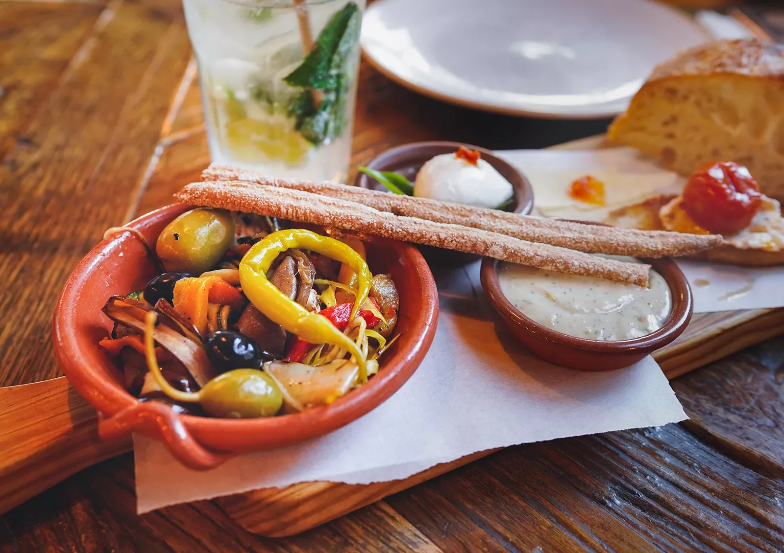 Wooden blank with breadsticks and a small bowl of a mixed vegetable salad