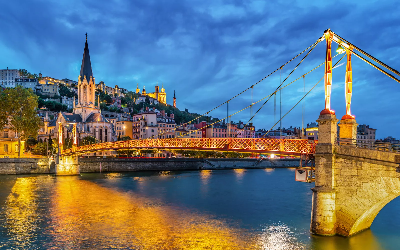 Illuminated suspension bridge leading to a rustic town