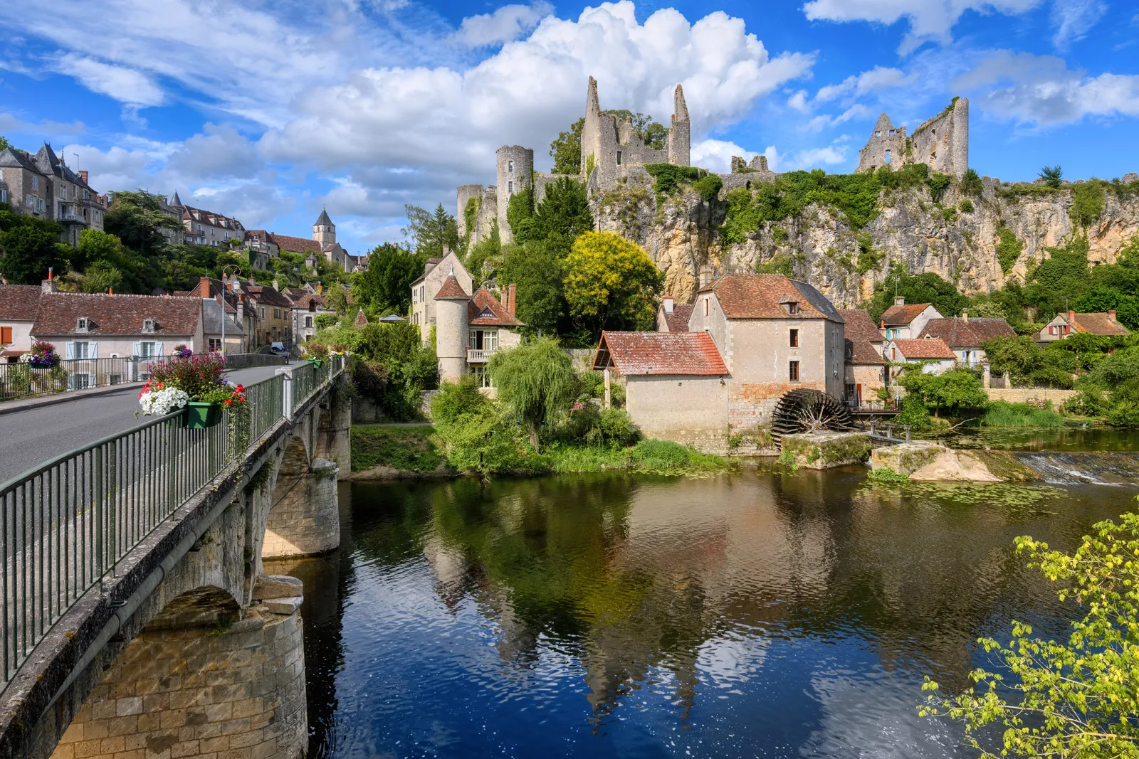 Bridge over a river with large, rustic ruins in the background