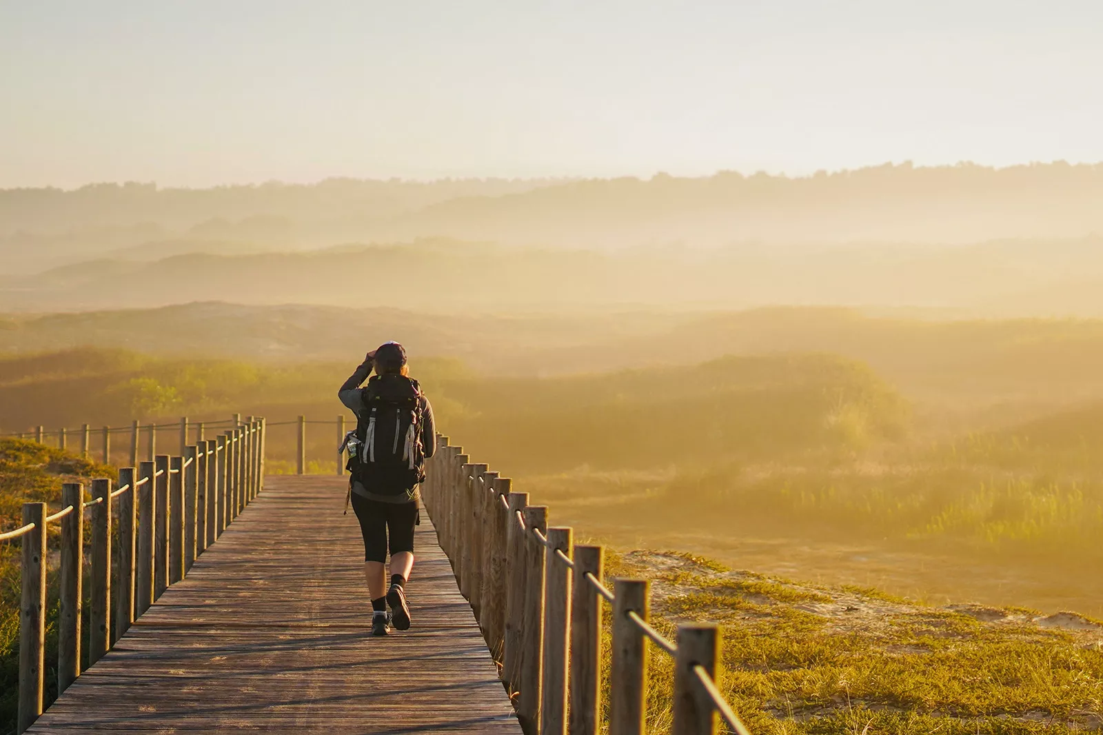 Person walking on a wooden bridge, in the middle of an open, grass field covered with fog