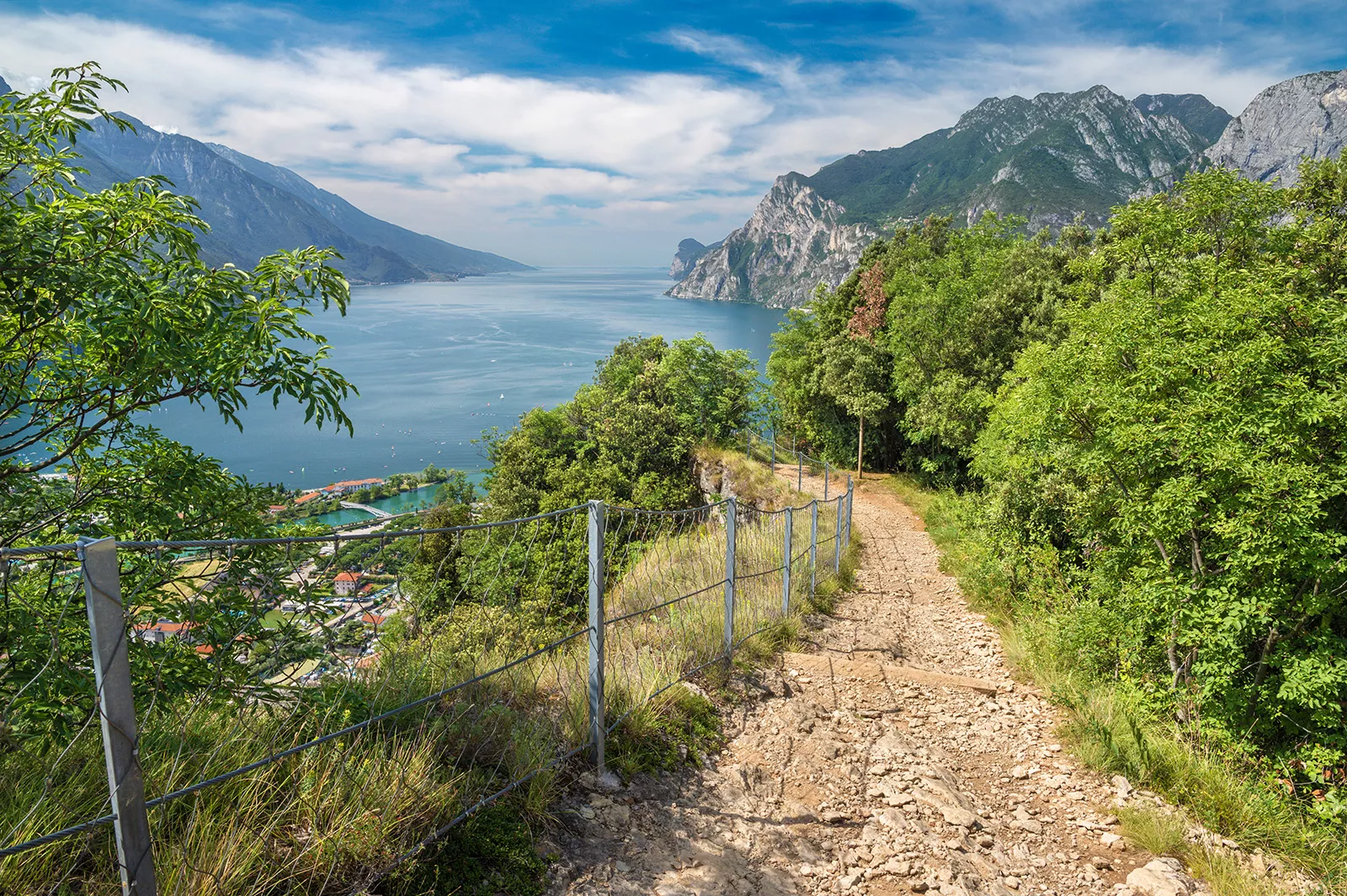 Descending dirt and gravel path surrounded by a fence and bushes