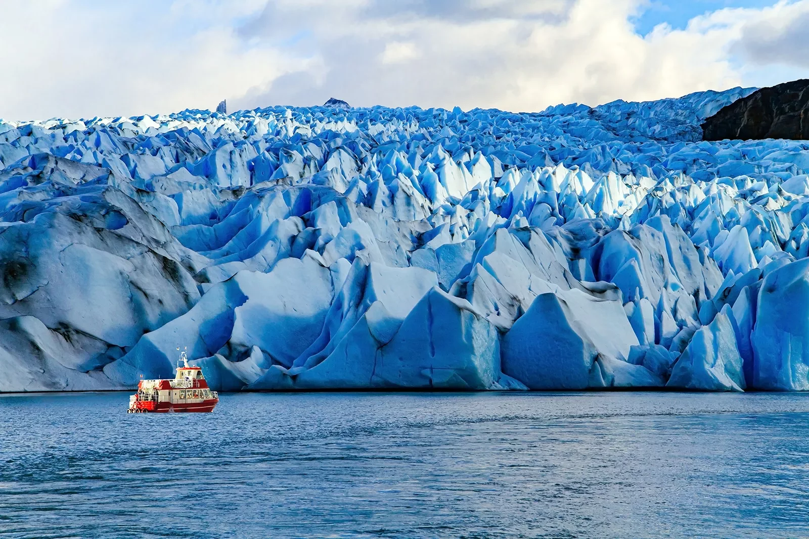 Jagged snow caps with a red and white boat traveling in front